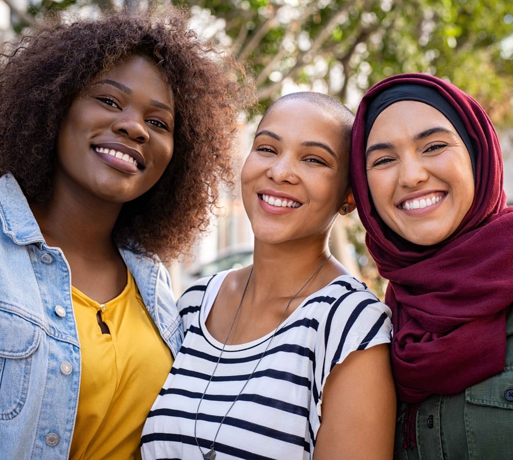 Three women from diverse backgrounds smiling together